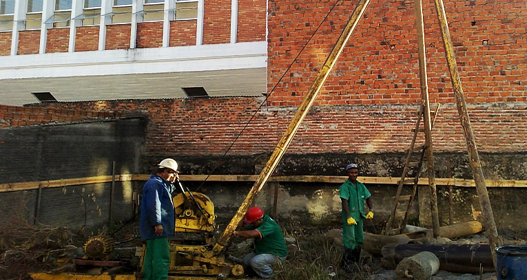 Equipe operando equipamento de estaca tipo Strauss ao lado de prédio de alvenaria